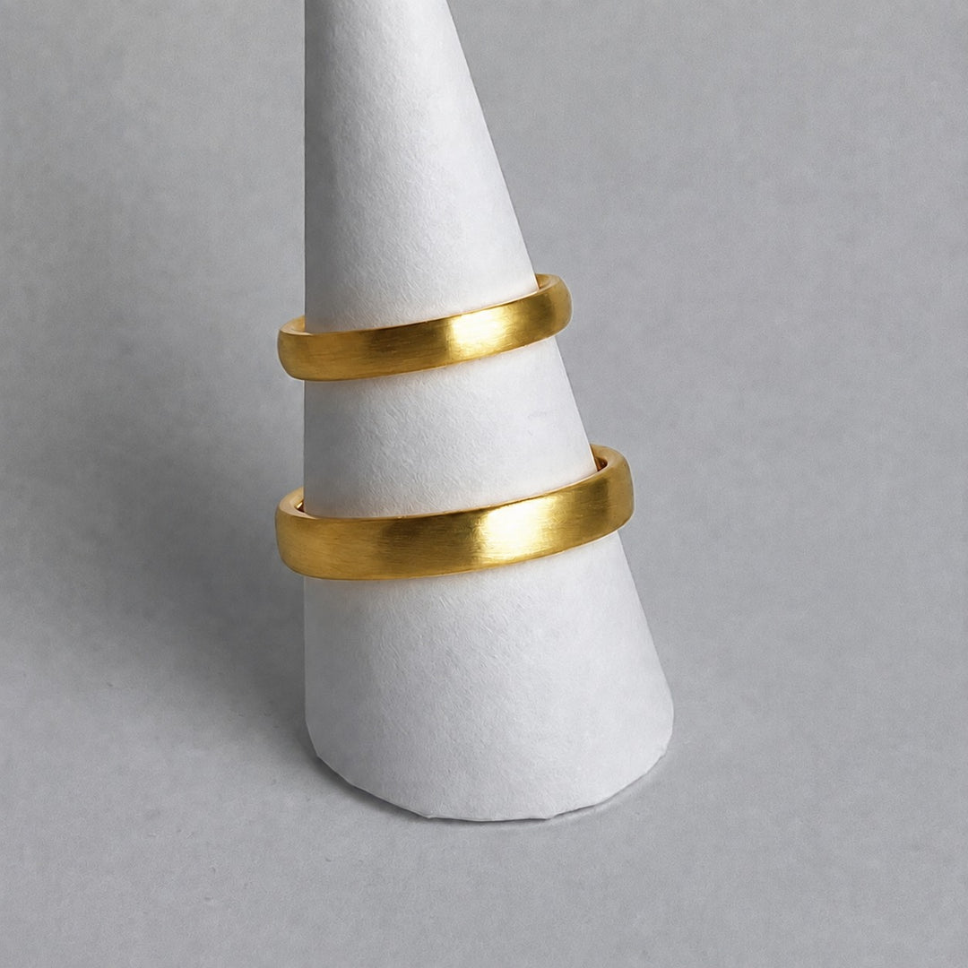Two curved 18ct yellow gold wedding rings shown together on a ring cone