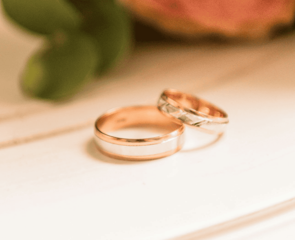 Two wedding bands in rose and white gold resting on a pale surface