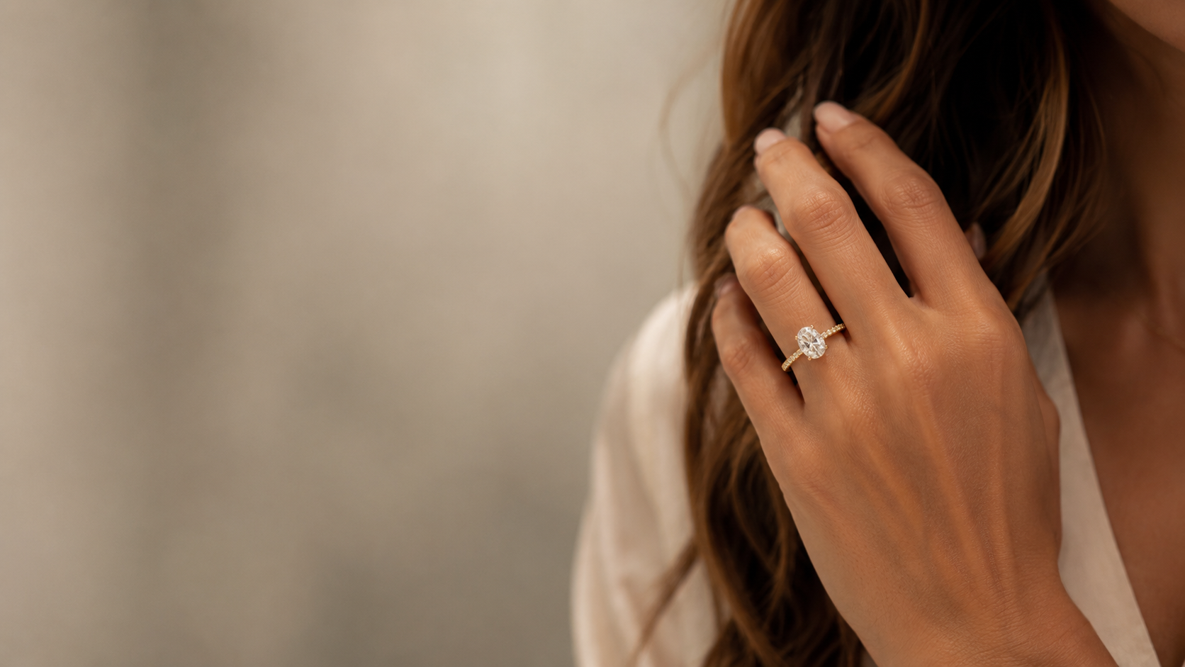 An oval solitaire engagement ring with a pavé band worn on the hand